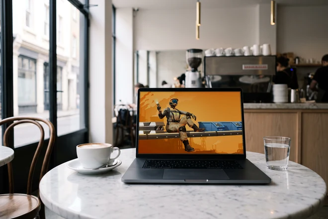 Dasselbe MacBook auf einer runden Marmorplatte im Café, daneben ein Cappuccino und ein Glas Wasser