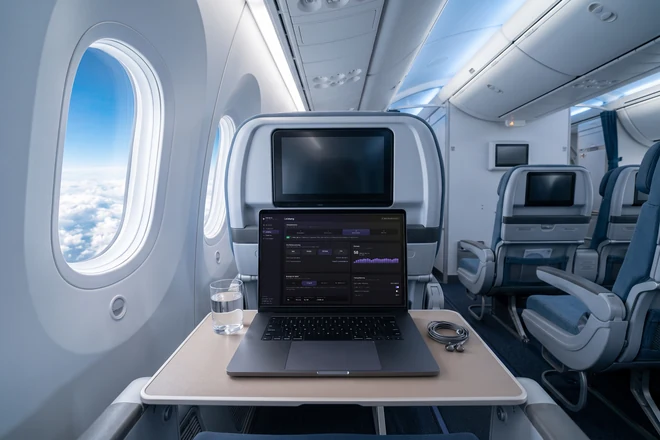 Dasselbe MacBook auf dem Tablett im Flugzeug, links das ovale Kabinenfenster