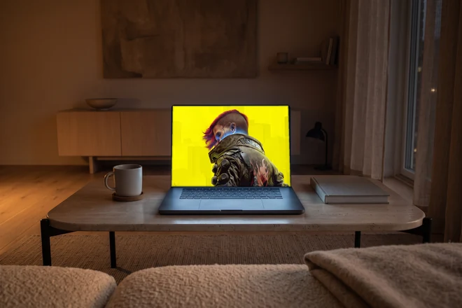 Dasselbe MacBook auf einem Travertintisch vor einem Sofa, daneben ein Becher auf einem Untersetzer