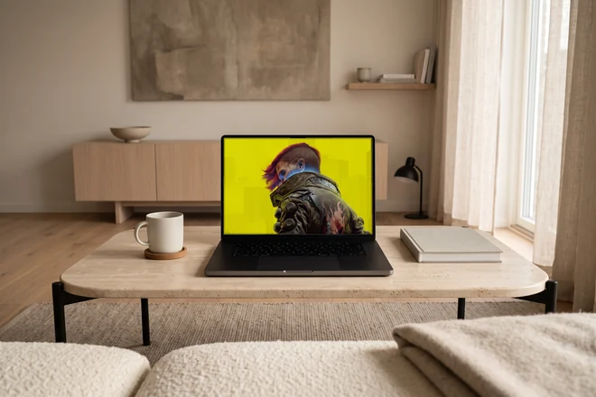 Dasselbe MacBook auf einem Travertintisch vor einem Sofa, daneben ein Becher auf einem Untersetzer