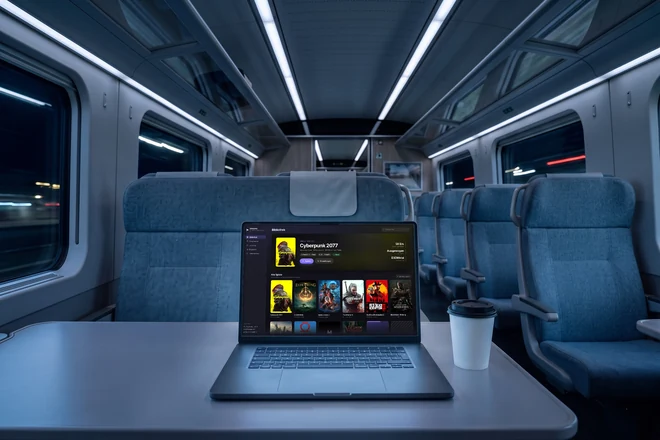 Dasselbe MacBook auf dem Klapptisch eines Zuges, draußen zieht die Landschaft vorbei
