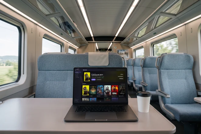 Dasselbe MacBook auf dem Klapptisch eines Zuges, draußen zieht die Landschaft vorbei